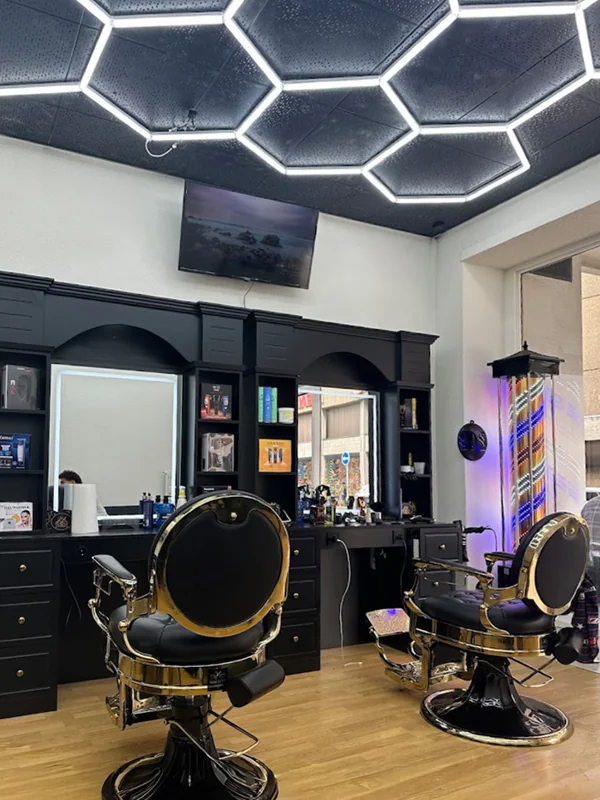 Sheroo-Salon mit schwarzen Barberstationen, goldenen Stühlen und geometrischer LED-Decke